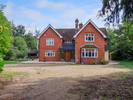 A brick detached house with a gravel driveway and surrounding trees at Brook Lodge in Pinewood near Ipswich