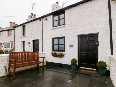 Front exterior of a white cottage with black doors and windows bench on patio at White Lilac Cottage in Brynsiencyn
