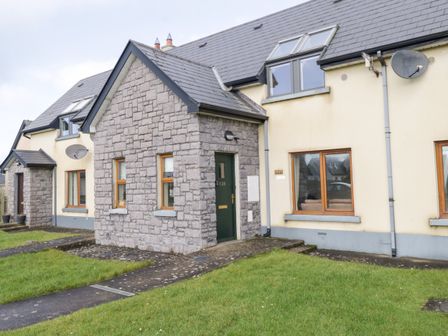 A stone and cream house with green door and windows next to a grassy lawn at Sea Breeze Holiday Home in Enniscrone County Sligo