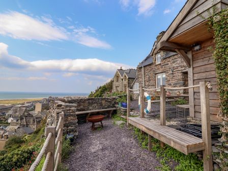 An outdoor seating area with stone buildings a fire pit and a view over rooftops to the sea at Pengarreg in Barmouth