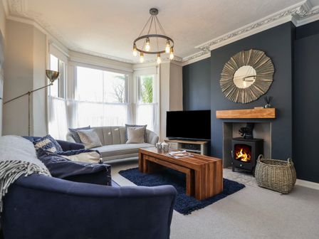 A living room with a bay window sofas a wooden coffee table a fireplace TV and a basket at First Light in Pakefield near Lowestoft