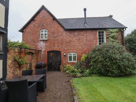 A patio area with a table and chairs outside a brick house with windows and a door at Millpond Bothy in Woolhope