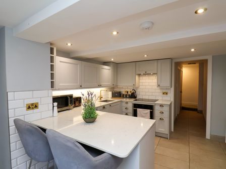 A kitchen with white cabinets a countertop with a plant two chairs a microwave toaster and a kettle at Kitty's Cottage in Whitby