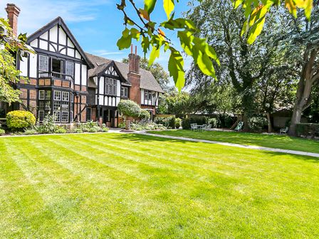 A large garden with a manicured lawn and trees in front of a Tudor style house at Tudor Grange in Bournemouth