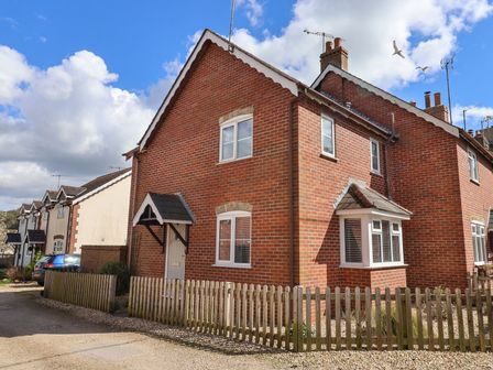 A brick semi detached house with white framed windows and a wooden fence in front at 8 Biddlecombe Orchard in Bridport