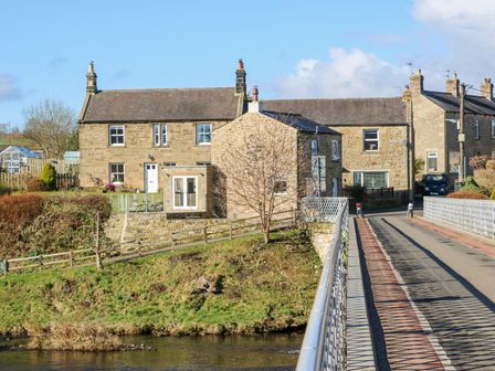 Stone houses near a small river with a narrow bridge leading to the road at Bridge End Cottage in Wark