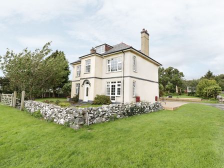 A two-story house with a stone wall surrounding part of the yard and grass outside at Tan Y Fron in Dyffryn Ardudwy