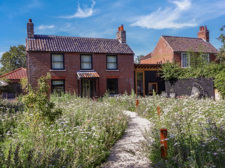 A garden path leading to two brick houses with tiled roofs and flower bushes at Oak Cottage in Somerleyton