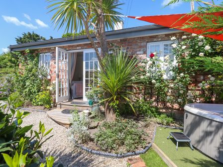 A garden with plants and a tree outside a brick house with open French doors at Sunset Cottage Swimbridge near Barnstaple