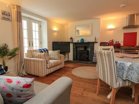 A living room with striped sofas a television a fireplace and a dining table with chairs at Quarter Deck in Salcombe