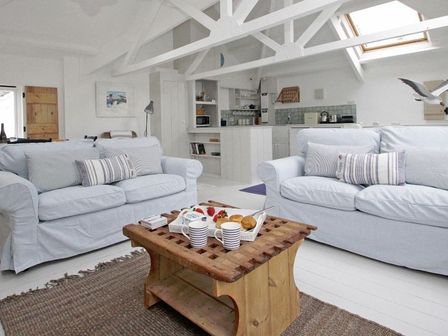 A living room with two sofas and a wooden coffee table and kitchen area at The Net Loft in Mousehole