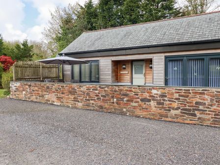 A building with stone wall patio umbrella and wooden door at The Stables in Ruthvoes near St Columb Major