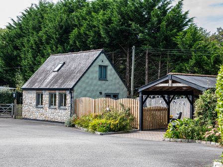 A stone and stucco house with a pitched roof next to a wooden carport and a garden with various plants at Little Willow in Ruthvoes near St Columb Major