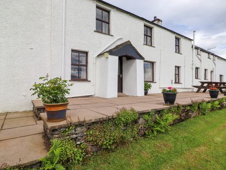 The exterior of a white building with a concrete patio featuring potted plants and a picnic table at Addyfield Farmhouse in Cartmel Fell near Bowland Bridge