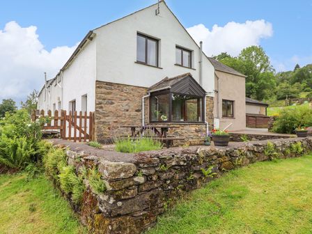 Exterior view of a stone and white plaster house with a wooden gate and stone wall at Addylea Cottage in Cartmel Fell near Windermere