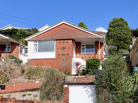 A brick bungalow with a white garage door and plants in front at Sandy Toes in Paignton