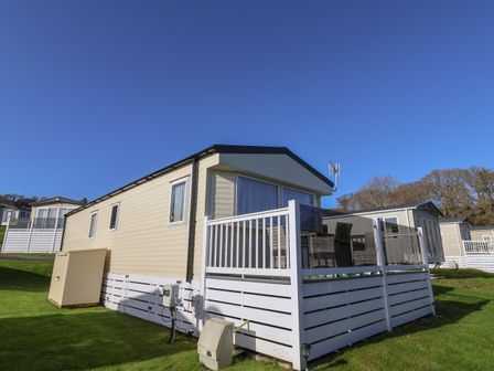 A beige mobile home with white railing and outdoor seating on a grassy area at Tri-Star House in Charmouth