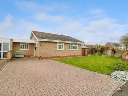 The exterior of a single-story brick house with a paved driveway and a lawn garden at Turnstone in Beadnell