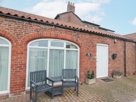 A brick exterior with arched windows white door two black chairs and a table at Fulmar Cottage in Flamborough