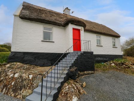 A white cottage with a thatched roof and a red door accessed by stairs surrounded by rocky ground at Aggrafard in Oughterard County Galway