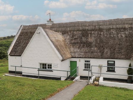 A white cottage with thatched roof and green door surrounded by grass at Ben Gower in Recess near Oughterard County Galway