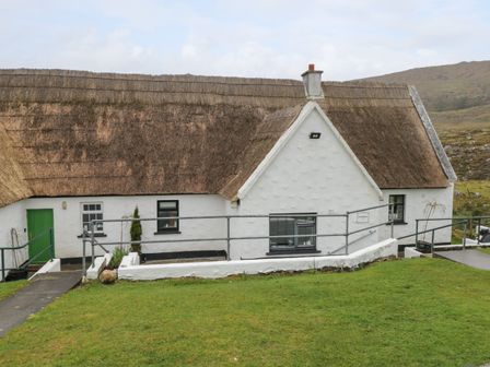 A white cottage with a thatched roof and green door with a grassy lawn in front at Ben Brack in Recess near Oughterard County Galway