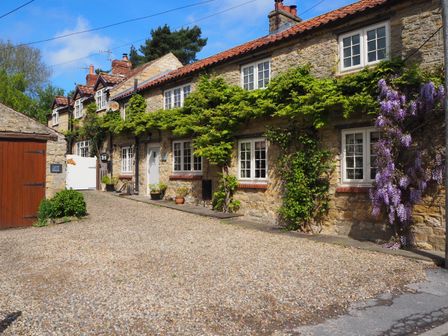 A stone cottage with multiple windows and climbing plants on the walls at Tillers Cottage in Ebberston