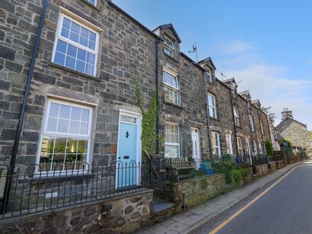 A row of stone terraced houses with white framed windows and pastel colored doors along a street at Glasfryn in Dolgellau