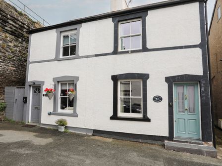 A white two-story cottage with black trim around windows and doors and a light blue door at Camellia Cottage in Conwy