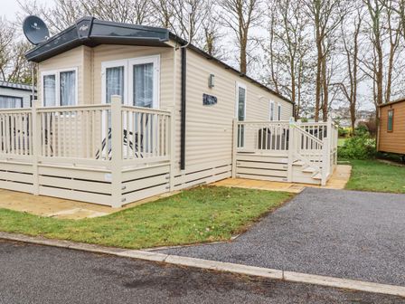 A beige mobile home with a white railing and steps surrounded by grass and trees at The Mermaid A04 in Par