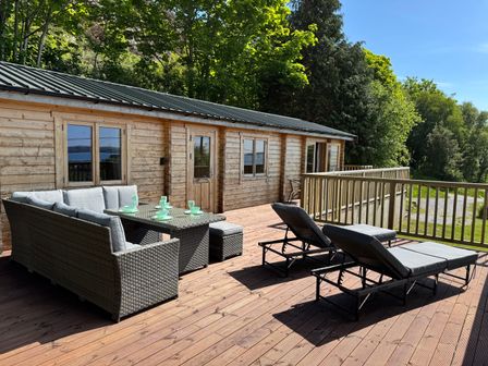 A wooden patio with outdoor furniture including a sofa set with a table and two lounge chairs at Northwood Lodge in Llanbedrog