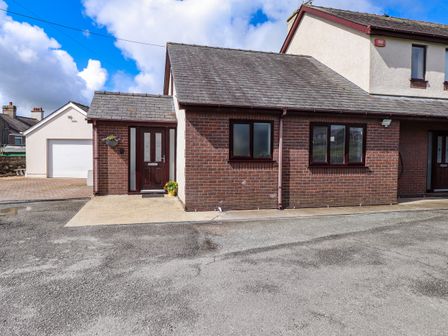 A brick and white exterior of a semi detached house with a driveway and a garage at The Annexe at Llwyfor in Llanrug