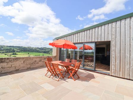 An outdoor patio with wooden table and six chairs under red umbrella adjacent to sliding glass doors and countryside view at Pit Close in Dalwood