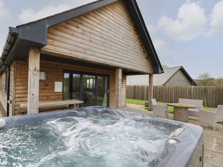 An outdoor patio with a hot tub wooden table bench and wicker chairs at Caban Dulas in Rhayader