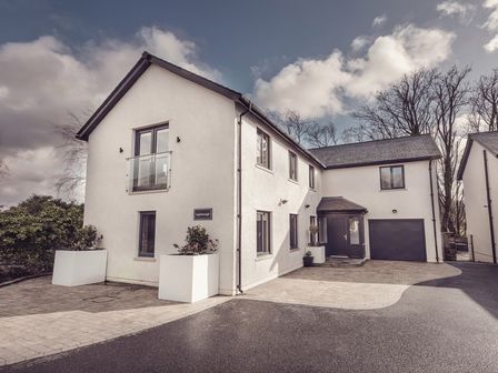 An exterior view of a two story white house with a driveway garage and plants in large pots at Ingleborough in Kirkby Lonsdale
