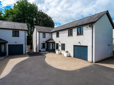 An exterior view of two white houses with driveways and garages surrounded by trees at Pen-y-Ghent in Kirkby Lonsdale