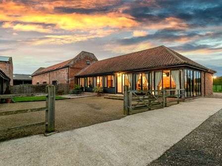A brick house with large windows and a tiled roof at sunset