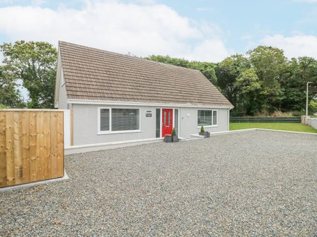 A house with a large gravel driveway and a red front door surrounded by trees at Wychwood in Hook near Haverfordwest