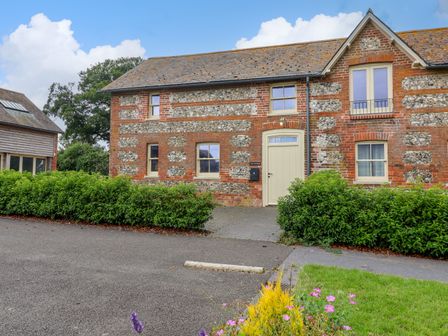 A brick and flint house with cream door and windows surrounded by green bushes at 8 Rookhaye in Salisbury