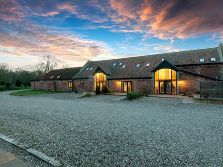 An exterior view of a long brick building with a tiled roof and large windows at dusk at Teal in Wheatacre