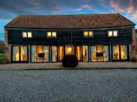 A two story building with black wooden exterior and large glass doors showing interior lights at Woodcock in Wheatacre
