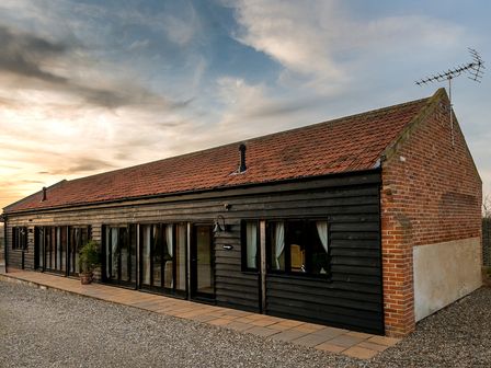 A black wooden barn with multiple glass doors and windows a tiled roof and an antenna at Partridge in Wheatacre