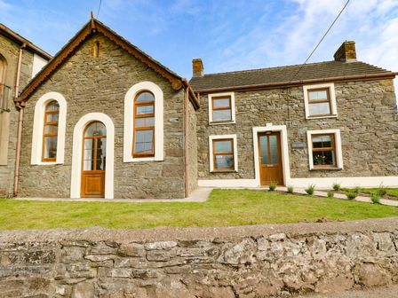 Stone cottage with wooden doors and windows and a grass lawn at Dalton Cottage in Llansaint