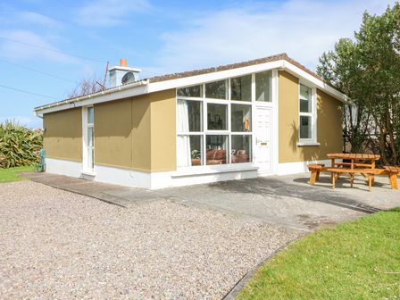 A single story house with large front windows and a wooden picnic table outside at The Sleepy Shell in Ballydavid County Kerry