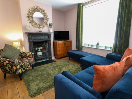 A living room with a blue sofa orange cushions a floral armchair green curtains a black fireplace and a wooden TV cabinet at Georgian Hideaway in Weymouth