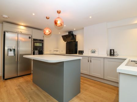A kitchen with an island, stainless steel refrigerator, built-in oven, and pendant lights at Swn Y Wylan in Morfa Nefyn