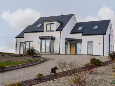 A modern white house with dark roof and multiple windows surrounded by a gravel driveway and landscaped garden at Moorhen House in Loughanure near Annagry County Donegal