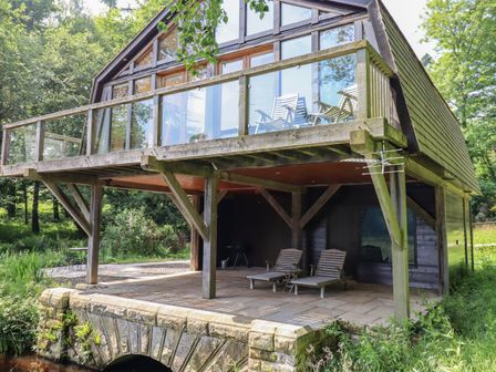 A wooden house with a balcony and outdoor chairs surrounded by trees at The Boathouse in Belford