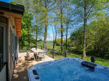 An outdoor deck with a hot tub and a dining table surrounded by trees at 23 Meadow Retreat in Dobwalls