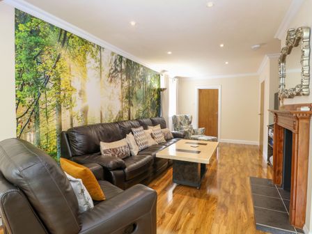 A living room with leather sofas a forest wall mural a wooden coffee table and a fireplace at Cedar Cottage in Blofield